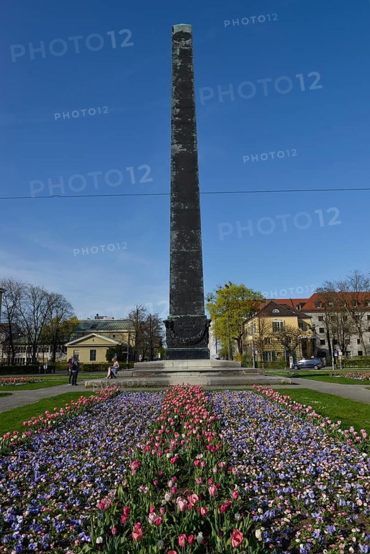 Obelisk with flower bed in front of houses roundabout