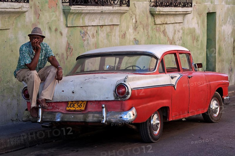 Cuban taxi driver sitting on a vintage taxi car