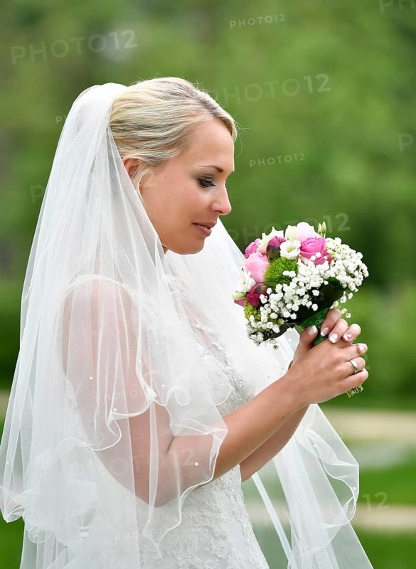 Bride in wedding dress with veil looking at bridal bouqet