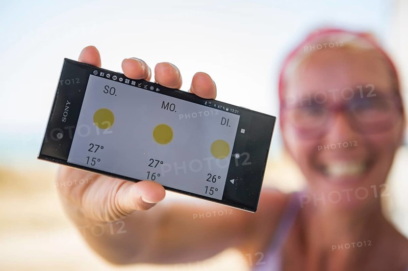 Laughing woman on the beach happy about sunny weather in the weather forecast on her smartphone