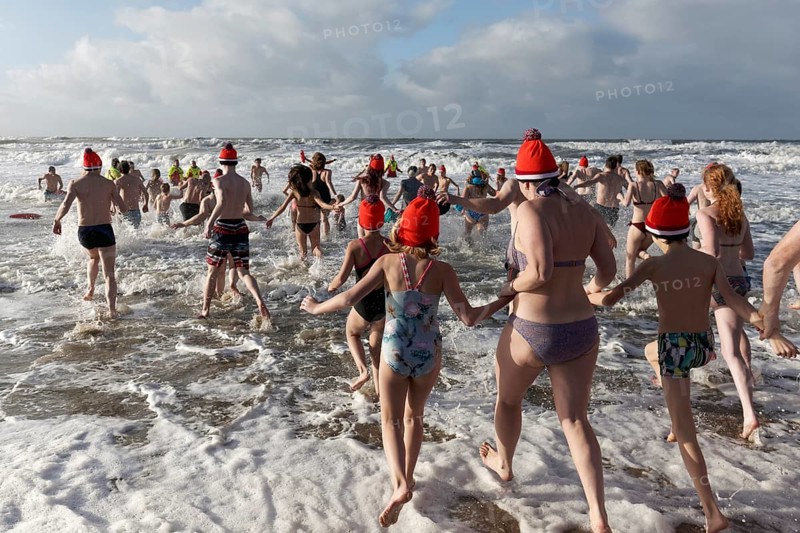 Many people in swimwear and Christmas hats run into the cold sea in winter