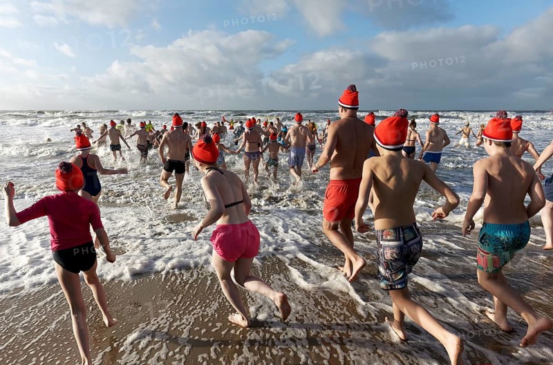 Many people in swimwear and Christmas hats run into the cold sea in winter
