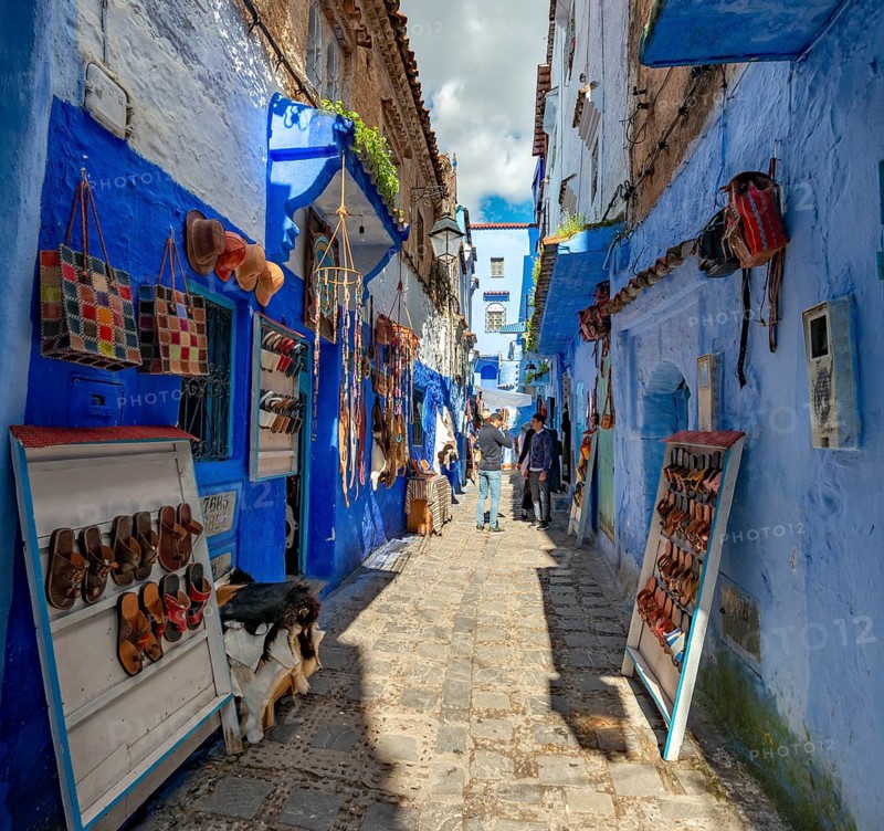Sale of leather sandals in narrow lane with blue houses