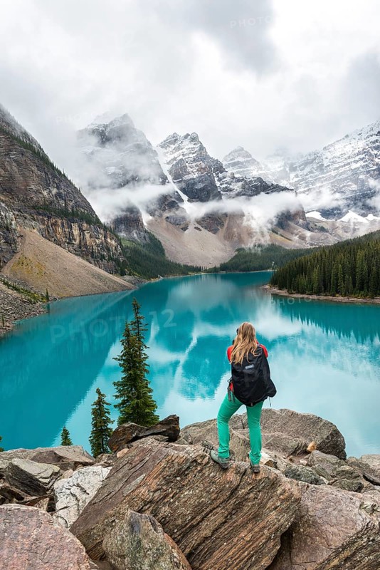 Young woman standing in front of a lake looking into mountain scenery