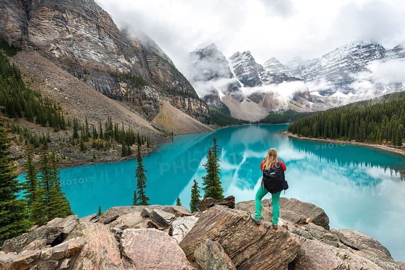 Young woman standing in front of a lake looking into mountain scenery