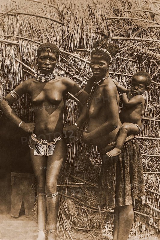 Two African women with a small child on their back in front of their hut