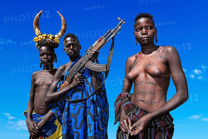 Young girls with decorative scars and man with Kalashnikov