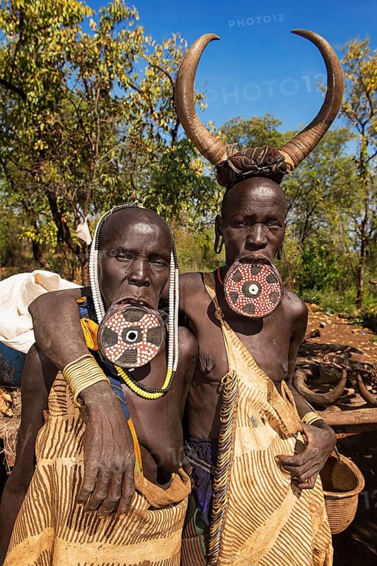Two women with large lip plates and horns as headdress