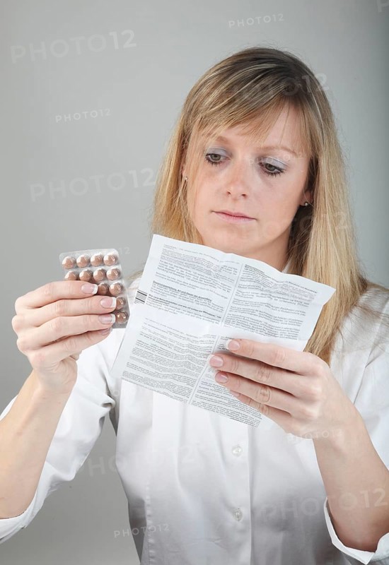 Young woman reading the package insert of a drug holding tablets in hand