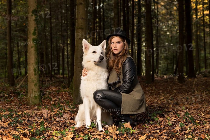 Blonde woman with white shepherd dog in the forest