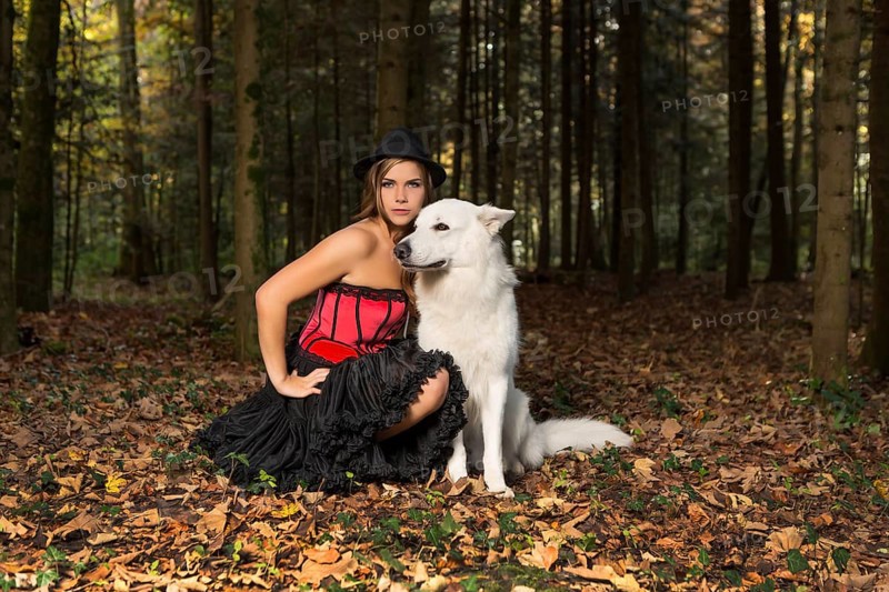 Blonde woman with white shepherd dog in the forest