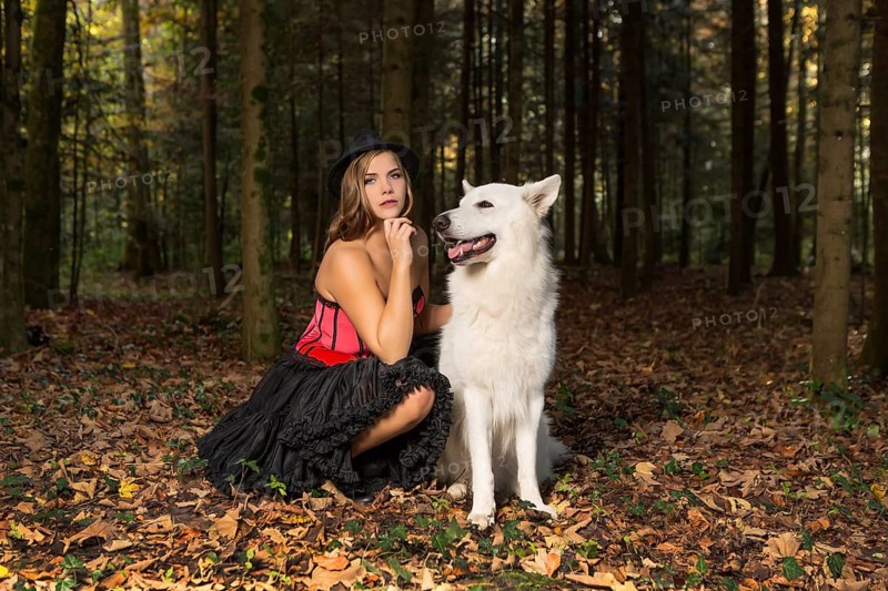 Blonde woman with white shepherd dog in the forest