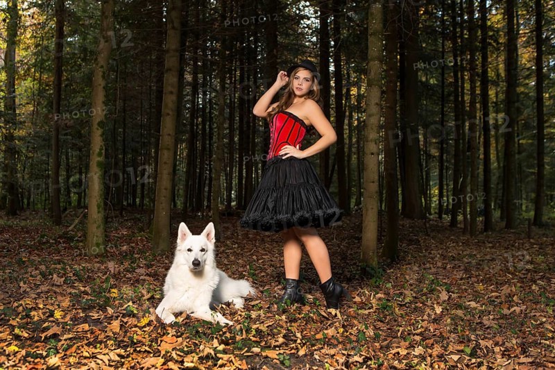 Blonde woman with white shepherd dog in the forest