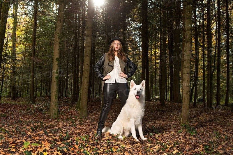 Blonde woman with white shepherd dog in the forest