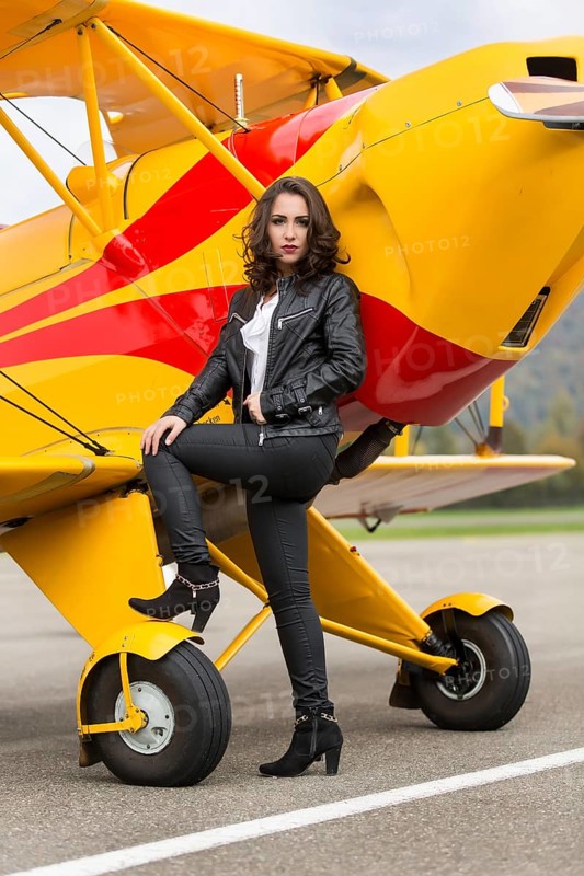 Young woman with leather jacket poses with yellow double-decker aviator