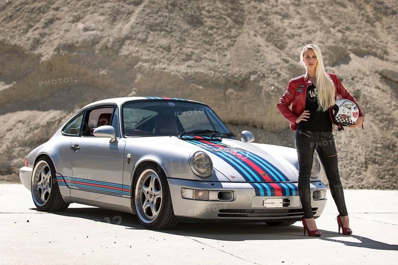 Young woman with long blonde hair poses with Porsche 911 Carrera 4