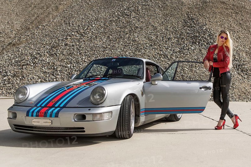 Young woman with long blonde hair poses with Porsche 911 Carrera 4