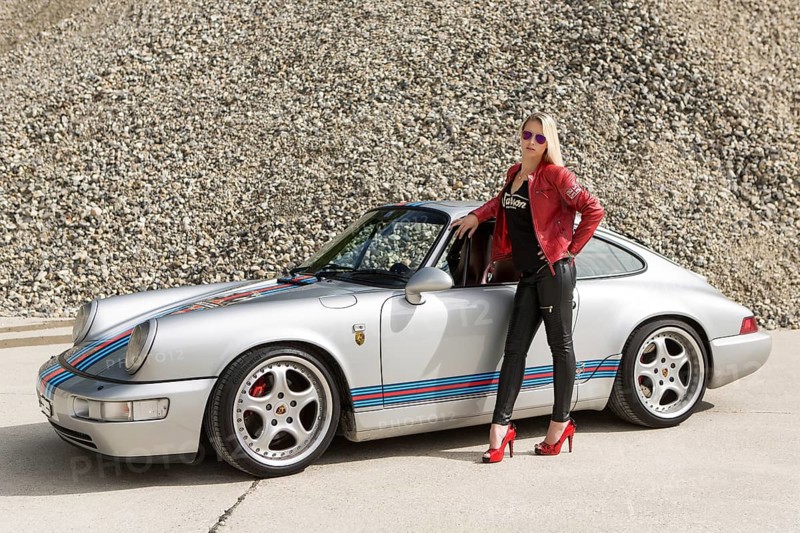Young woman with long blonde hair poses with Porsche 911 Carrera 4