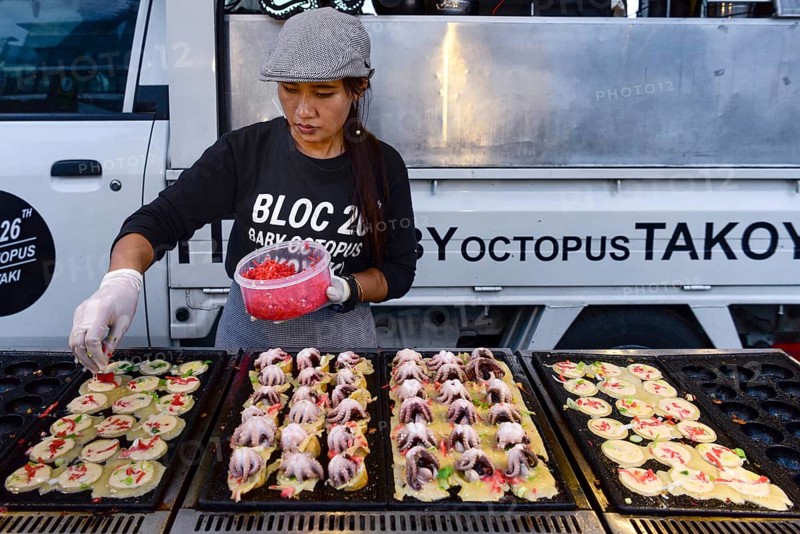 Woman sells baby octopus from grill at a food stall