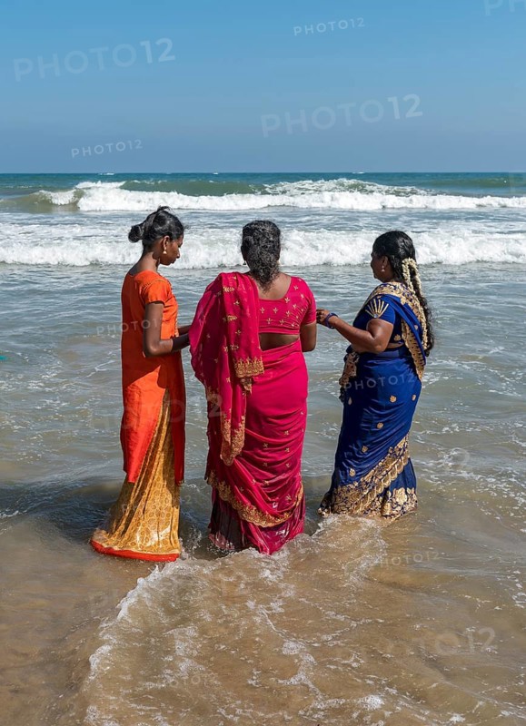 Three women in sari dress stand in ocean on the Bay of Bengal coast
