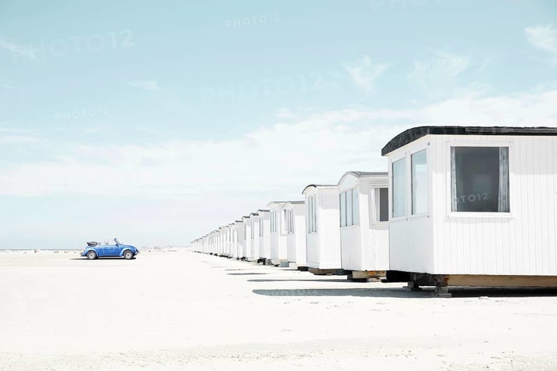 Blue VW Beetle cabriolet faces white beach huts
