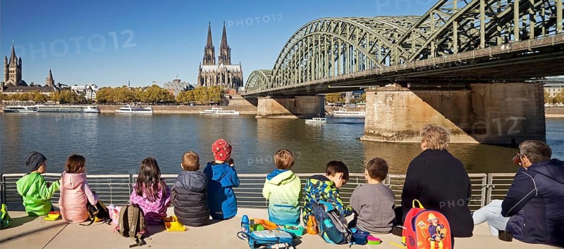 Children's group having a picnic on the Rhine Boulevard with Cologne Cathedral and Hohenzollern Bridge in the background