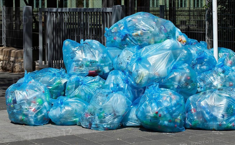 Full light blue garbage bags with plastic garbage on one heap