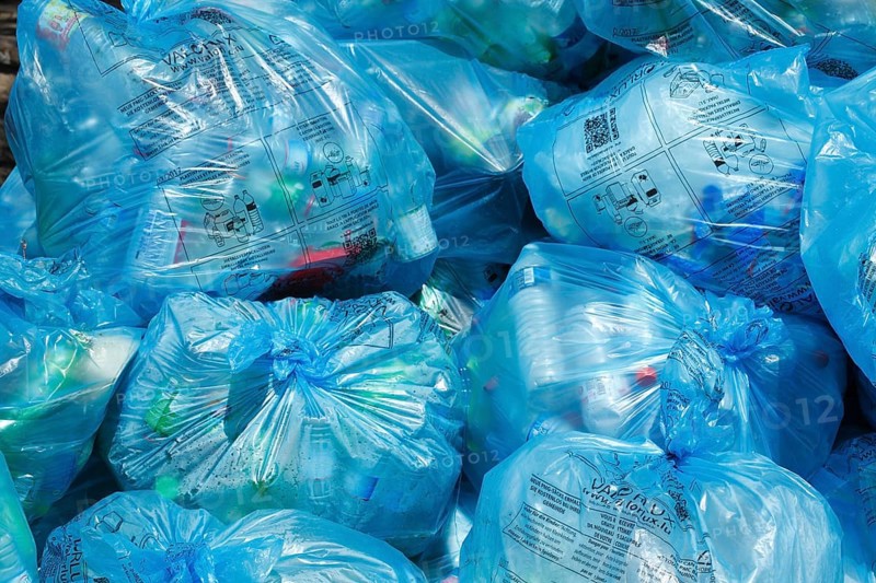 Full light blue garbage bags with plastic garbage on one heap