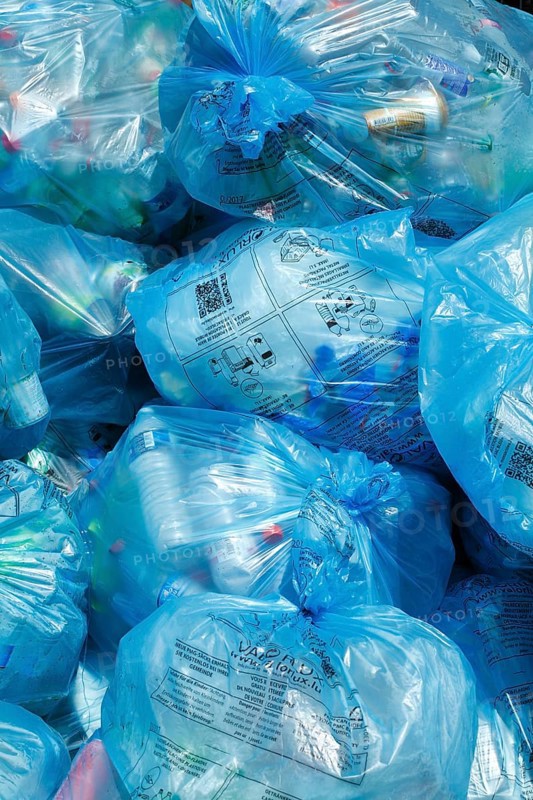 Full light blue garbage bags with plastic garbage on one heap