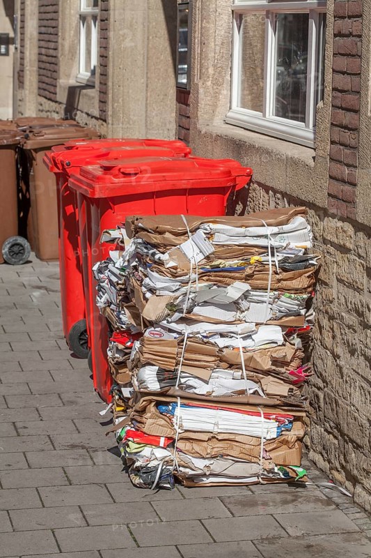 Red bins for waste glass and stacks of waste paper