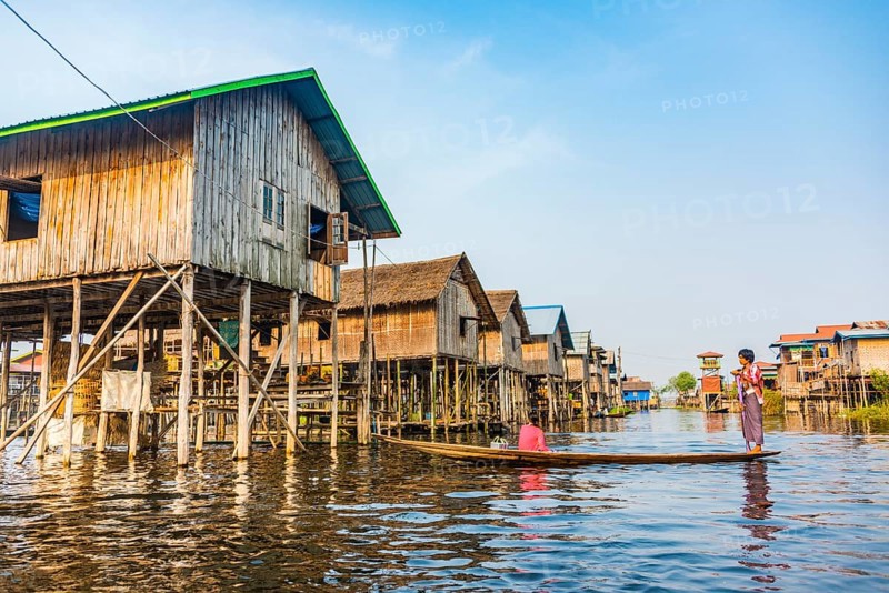 Wooden boat with locals in front of traditional stilt houses on Inle Lake