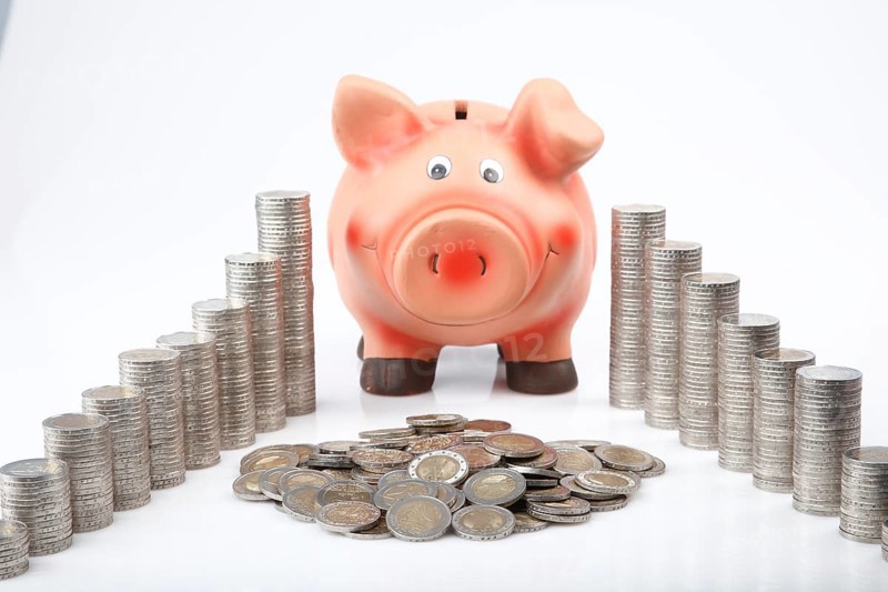 Piggy bank behind heaped and stacked coins