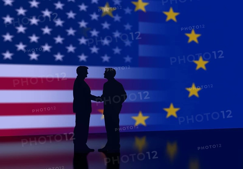 Two businessmen shaking hands in front of USA flag and EU flag