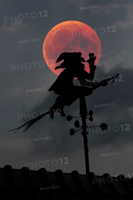 Blood moon over the roof of a house with weather vane with weather witch