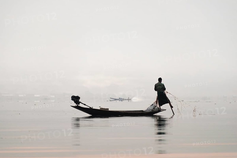 Local fisherman leg rower with wooden boat in the morning fog