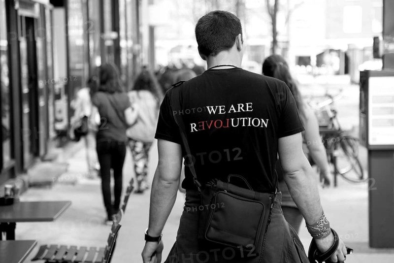Man walking down the street wearing a T-shirt with the inscription We Are Revolution
