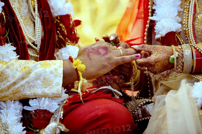 Bride with bridal jewelry and henna decoration on her hand attaches ring to the grooms finger at traditional religious ceremony at a Hindu wedding