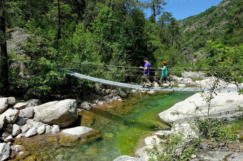 Hikers on a suspension bridge across the river Bonifatu at the long-distance trail Tra Mare e Monti and GR20