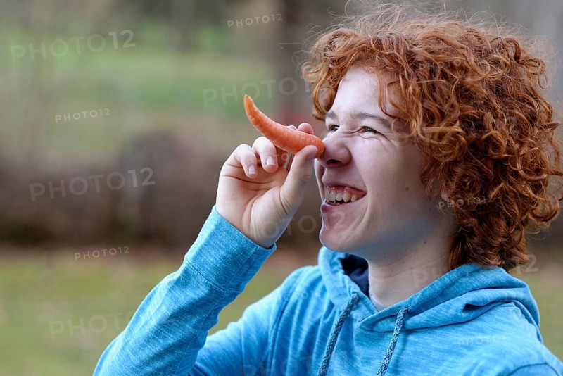 Teenager using a carrot as a long nose
