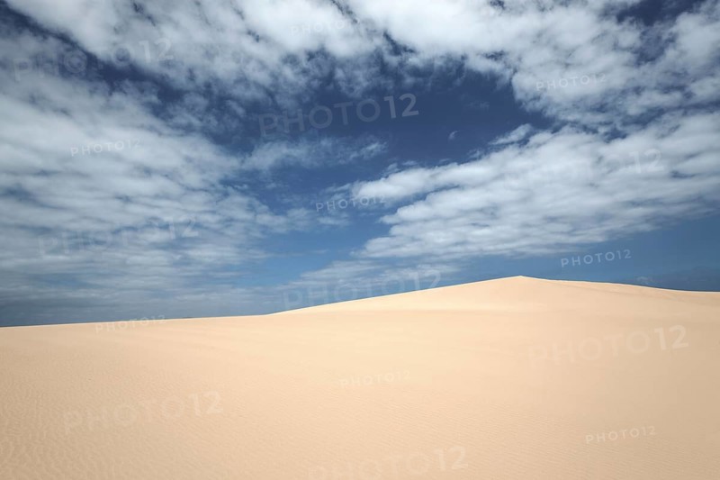 Sand dunes under blue sky with clouds
