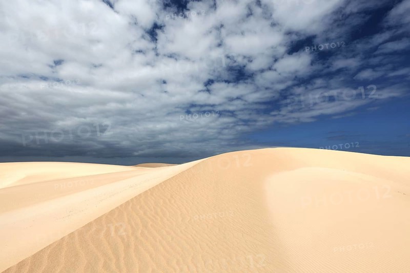 Sand dunes under blue sky with clouds