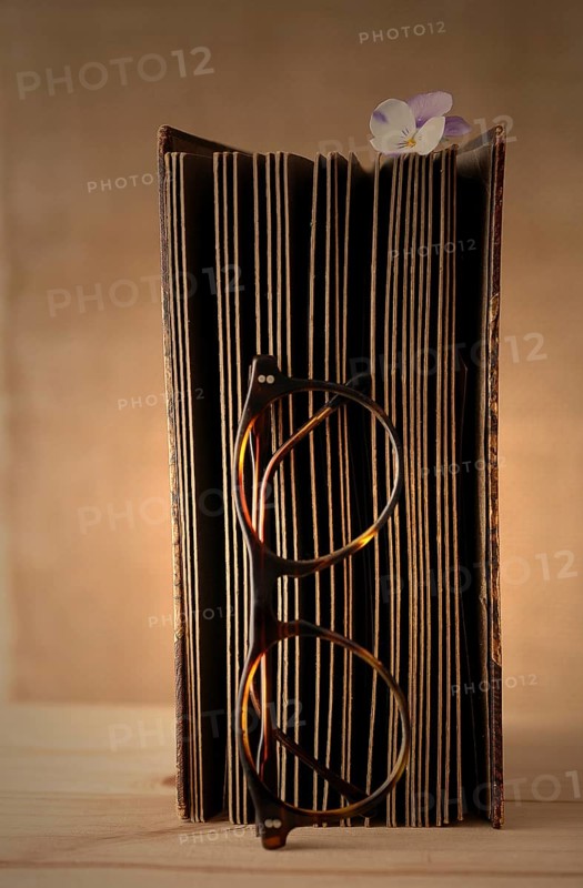 Old book with reading glasses and a horned violet