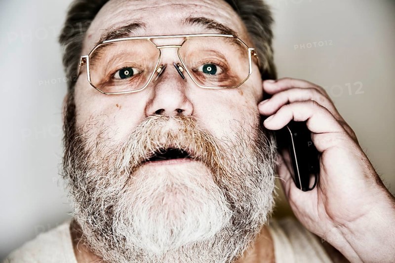 Senior with a full beard and glasses in undershirt on the smartphone