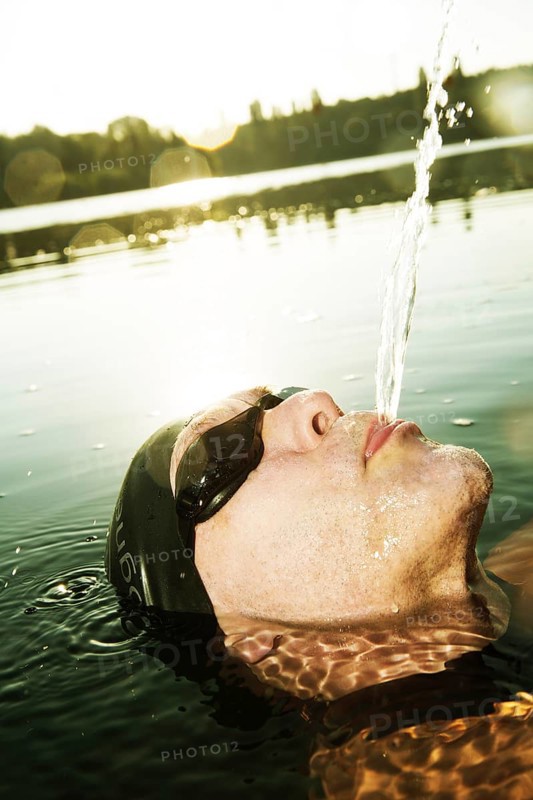 Man with swimming goggles spitting water in lake