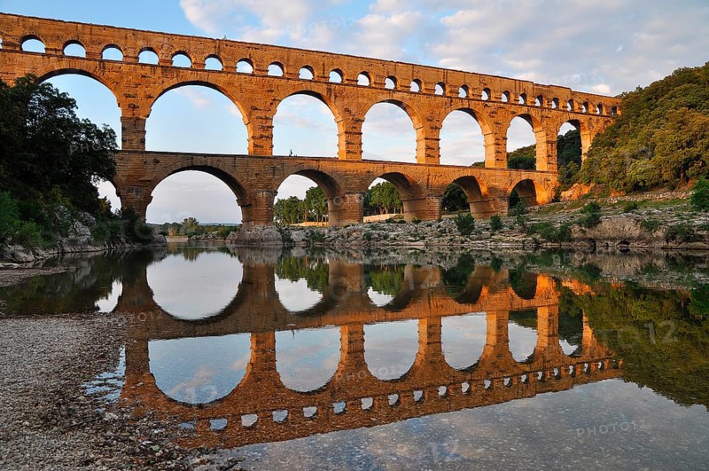 Roman aqueduct Pont du Gard reflected in the Gardon river in the evening