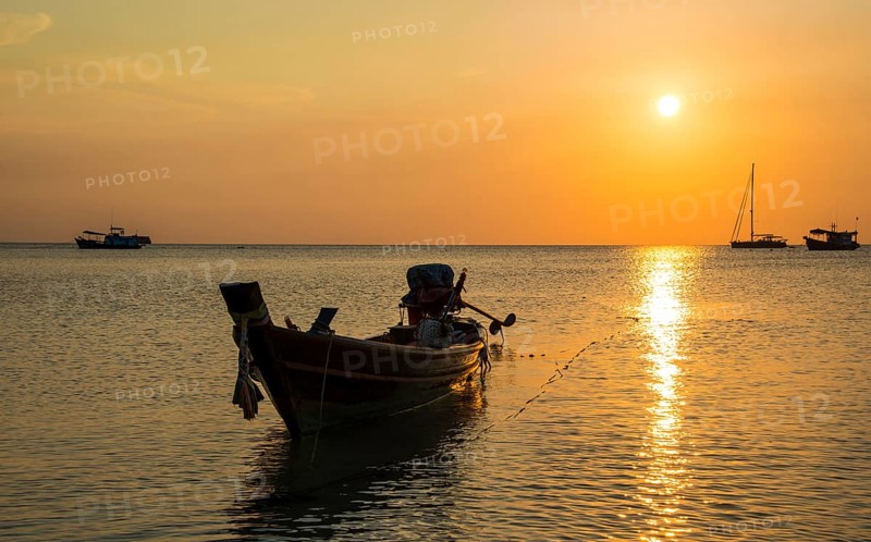 Long-tail boat in sea at sunset