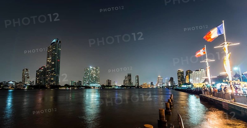 River promenade in the evening with a Ferris wheel and the skyline on the river Mae Nam Chao Phraya
