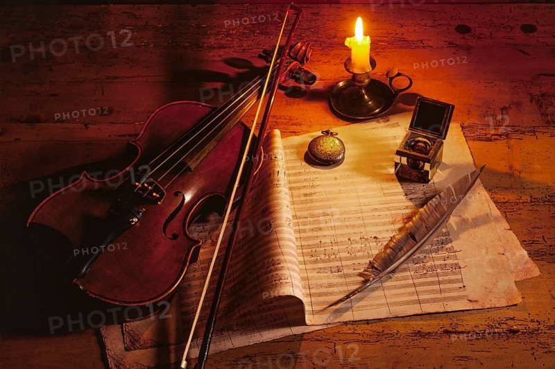 Violin with music sheet and quill by candlelight