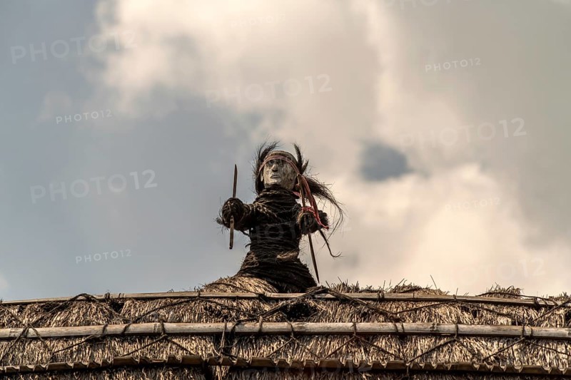 Figure on the roof of a thatched wooden house