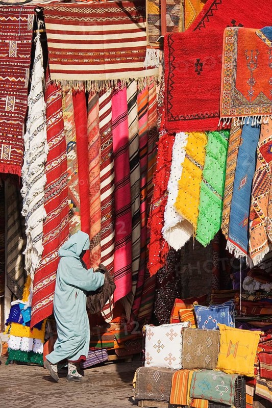 Woman in front of a shop with colourful carpets in the souks of Marrakesh